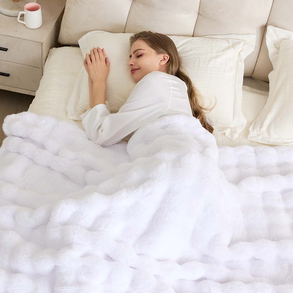 Person relaxing under a soft cream textured throw on a sofa in a bright neutral living room